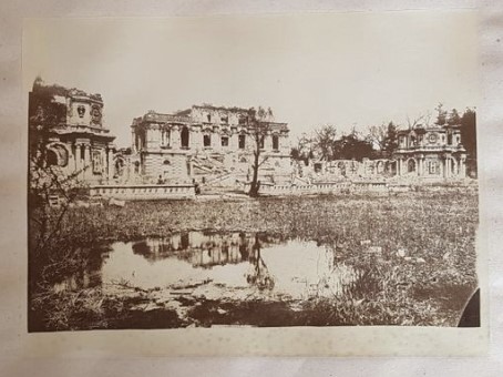 Fig 8. The 'Palace of the Delights of Harmony' (Xieqiqu), Yuanmingyuan, viewed from the south, across the weed choked pool, reflecting the ruins of the palace. Two men are posed by the balustrade around the pool. This print was made with an indented rounded corner mask (i.e. a 'signature' of Moore's) and captioned: ‘Bâtiment principal construit par […] a Yuen Ming Yuen / Etat 1879 d'après Moore / 26 / 19’. This is a key photographic print/captioning, connecting Moore's name with the rounded corner mask, strategically placed people, as well as showing more from his (lost) negative than other prints. A well composed and frequently reproduced photograph, its punctum, for many, being the reflection of the ruin in the water. Source: Part of Lot 2, in an auction by Tessier &amp; Sarrou et Associés, Paris, on 17 December 2018.